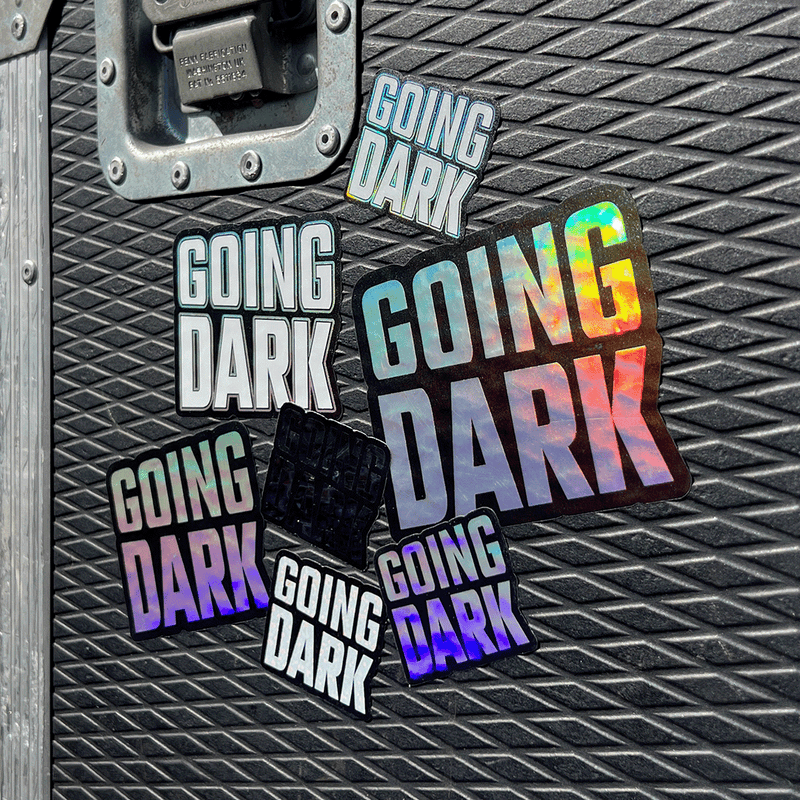 A flightcase featuring the Going Dark Special Edition 7-Piece Sticker Set. The set includes a variety of unique finishes, featuring holographic, mirror, and glitter designs that catch the light in all the right ways, creating a dynamic, eye-catching effect. The stickers are displayed on the lid of the flightcase, with bold, edgy graphics, including abstract patterns, logos, and stylised text, adding a custom, artistic flair.