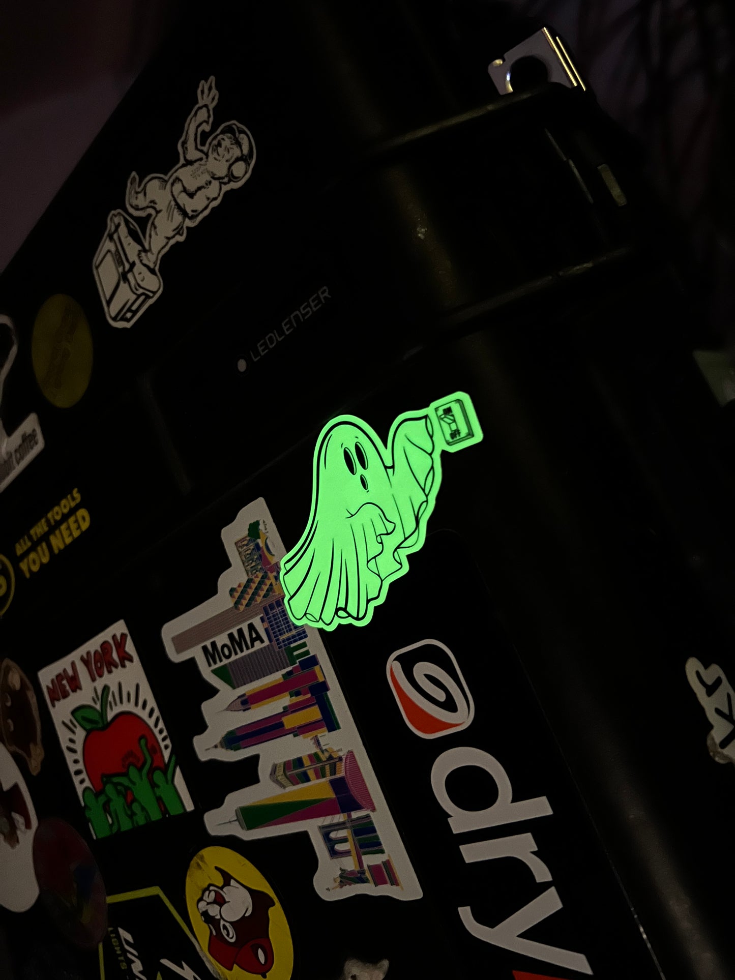 Glowing green sticker on a black surface with various other stickers.
