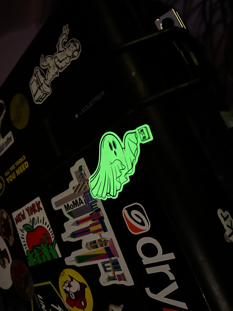 Glowing green sticker on a black surface with various other stickers.